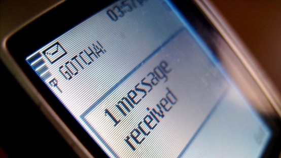 A close-up, angled shot of a retro mobile phone screen displaying a pixelated envelope icon of an SMS, the text "GOTCHA!", and a notification reading "1 message received."